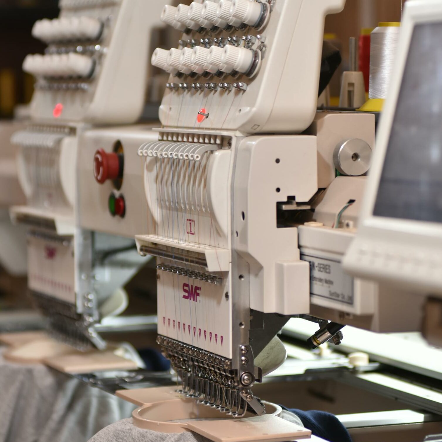 Close-up of automated industrial sewing machines stitching fabric in a factory setting.